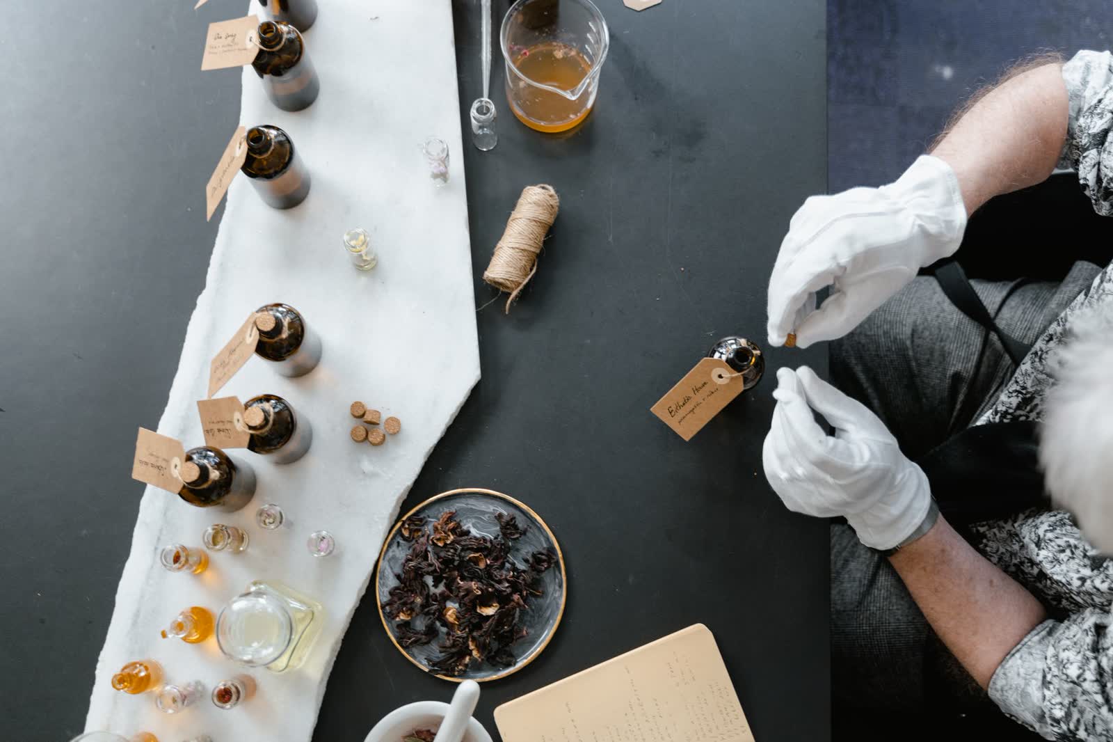 A perfumer's bench — gloved hands weighing an accord among vials